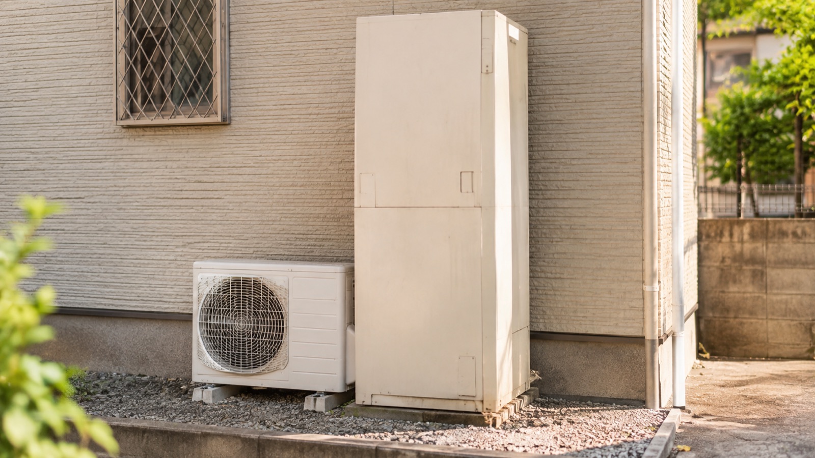 住宅の外壁横に設置された、年季の入ったエコキュートの貯湯タンクと室外機